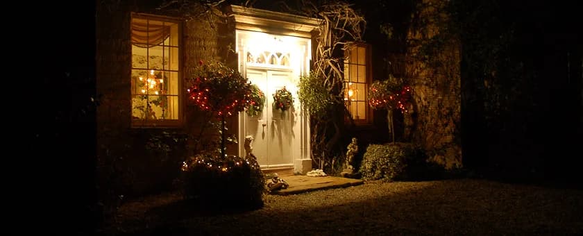 A warmly lit Upper Court cottage entrance decorated for Christmas at night