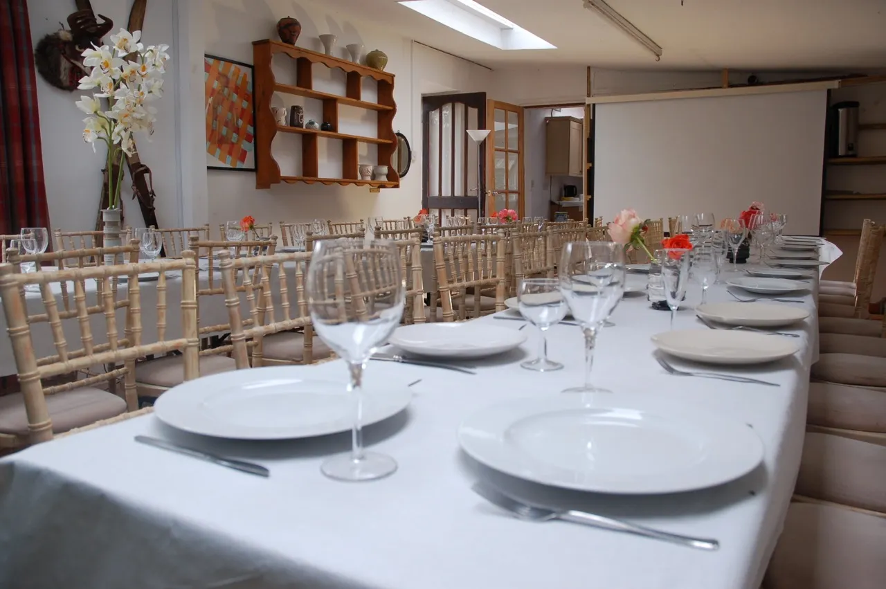 Long table set with white linen, plates and glasses in the Gallery at Upper Court, ready for a group meal