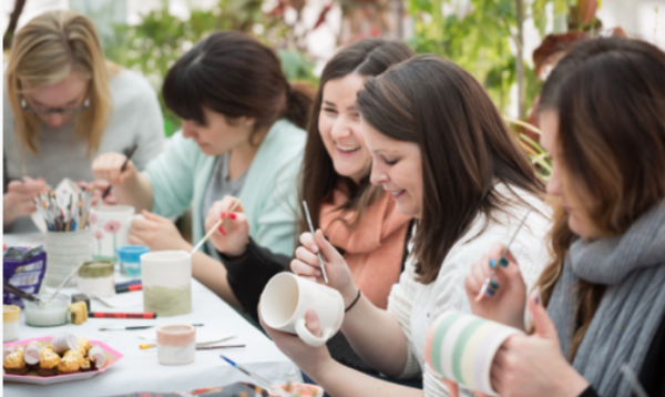 A photograph of a group of smiling friends painting mugs together